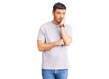 Ayılı yakışıklı genç adam rahat bir tişört giyiyor. Yorgun ve bunalımda gibi görünüyor. Kollarını kavuşturmuş.. 