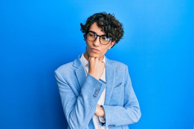 İş ceketi ve gözlük takan İspanyol genç adam ciddi bir yüzle eli çeneli soruyu düşünüyor, kafa karıştırıcı bir fikir hakkında düşünceli. 