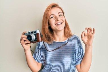 Beyaz kadın elinde antika bir kamera tutuyor parmaklarıyla imza atıyor, gülümsüyor ve mükemmel bir sembol oluşturuyor. 