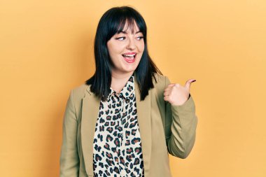 Genç İspanyol kadın iş kıyafetleri içinde gülümseyen, gülen yüzlü başparmağıyla yan tarafı işaret ediyor.. 