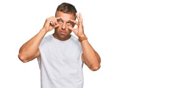 Yakışıklı, beyaz tişört giyen, gözlerini parmaklarıyla açmaya çalışan, uykulu ve yorgun bir adam. 