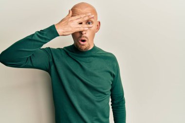 Sakallı, balıkçı yaka kazaklı, kel bir adam. Şok olmuş, yüzünü ve gözlerini kapamış, parmaklarından korkuyla bakıyor. 