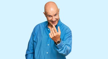 Orta yaşlı, kel, sıradan giyinmiş bir adam, el kol hareketi yaparak, mutlu bir şekilde karşılamaya ve gülümsemeye davet ediyor. 