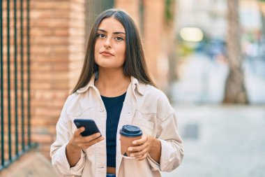 Akıllı telefon kullanan ve şehirde kahve içen ciddi bir suratı olan genç İspanyol kız..