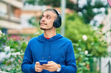 Genç İspanyol adam şehirde akıllı telefon ve kulaklık kullanarak mutlu gülümsüyor..