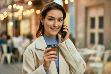 Genç İspanyol kadın akıllı telefondan konuşuyor ve şehirde kahve içiyor..