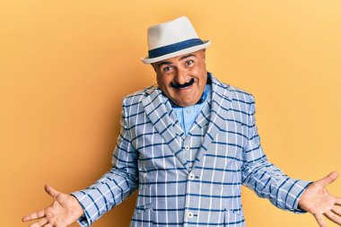 Klasik ve zarif moda tarzı olan bıyıklı olgun bir orta doğulu. Kolları ve elleri havada, kafası karışık bir ifade takınıyor. şüphe kavramı. 