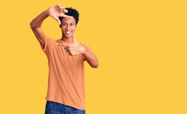 Gündelik kıyafetler giyen, gülümseyen ve mutlu yüzlü elleri ve parmakları olan genç Afro-Amerikan bir adam. yaratıcılık ve fotoğrafçılık kavramı. 