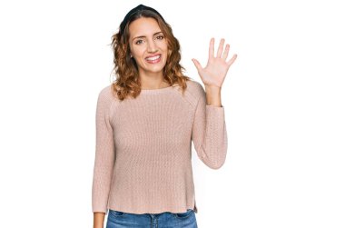 Güzel, genç, beyaz bir kadın günlük süveter giyiyor ve beş numarayı gösterip gülümserken kendinden emin ve mutlu.. 