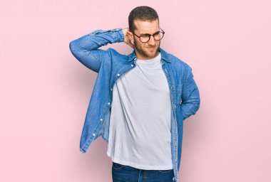 Günlük kıyafetler giyen, boynu ağrıyan, eli boynuna dokunan, kas ağrısı çeken genç beyaz bir adam. 