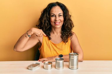 Konserve yiyeceklerle dolu orta yaşlı güzel bir kadın gülümseyen, mutlu ve gururlu birini işaret ediyor. 