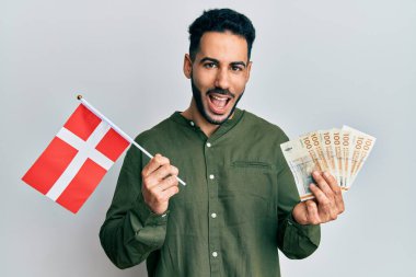 Danimarka bayrağı ve krone banknotları tutan genç İspanyol adam kahkahalarla gülüyor.. 