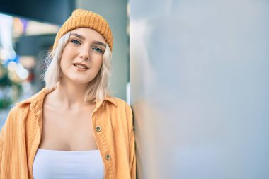 Genç sarışın kız gülümsüyor, mutlu bir şekilde şehirde duruyor..