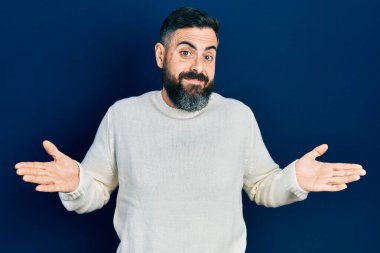 Sıradan kıyafetler giyen, elleri ve kolları havada, kafası karışmış genç İspanyol bir adam. şüphe kavramı. 