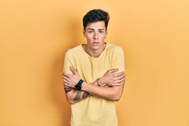 İspanyol asıllı genç adam, günlük sarı tişört giyiyor. Kış soğuğu için titriyor ve donuyor. Yüzünde üzgün ve şok ifadesi var. 