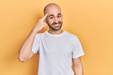 Young bald man wearing casual white t shirt smiling pointing to head with one finger, great idea or thought, good memory 