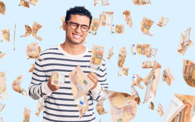 Gündelik kıyafetler ve gözlük takan İspanyol yakışıklı genç adam başarı için heyecanlanıyor kolları havada ve gözleri kapalı zaferi kutluyor. Kazanan konsept.