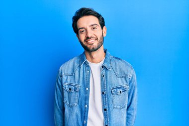 Yüzünde mutlu ve havalı bir gülümseme olan sıradan kıyafetler giyen genç İspanyol bir adam. şanslı kişi. 