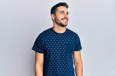 Latin kökenli genç bir adam günlük giysiler giyiyor, rahat bir görünüm takınıyor, doğal bir yüz ifadesi ve kendinden emin bir gülümsemeyle poz veriyor.. 