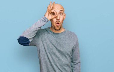 Bald man with beard wearing casual clothes doing ok gesture shocked with surprised face, eye looking through fingers. unbelieving expression. 