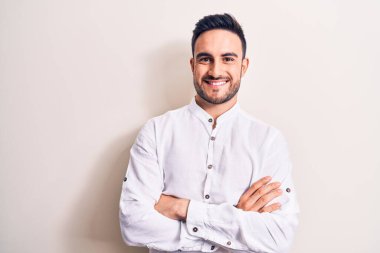 Sakallı, sıradan tişörtlü, beyaz arka planda duran, kollarını kavuşturup kameraya gülümseyen genç yakışıklı bir adam. Pozitif kişi.