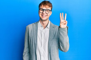 Zarif kıyafetler giyen ve gözlük takan beyaz bir adam üç numaralı parmaklarıyla gülümseyerek kendinden emin ve mutlu bir şekilde işaret ediyor.. 