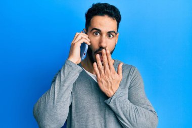 Genç İspanyol bir adam akıllı telefonda konuşuyor. Ağzını eliyle kapatıyor. Şok geçiriyor ve hata yapmaktan korkuyor. şaşırmış ifade 