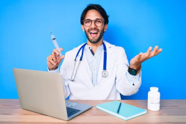 Yakışıklı İspanyol doktor klinikte elinde şırıngayla zaferi kutluyor. Gülümsüyor ve ellerini kaldırıyor. 