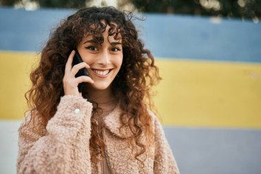 Genç İspanyol kadın gülümsüyor. Şehirdeki akıllı telefondan konuşuyor.