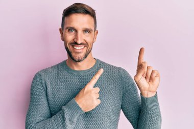 Sakallı, sıradan bir kazak giyen, gülümseyen ve kameraya bakan yakışıklı bir adam.. 