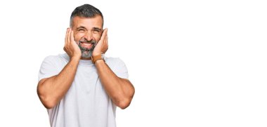 Orta yaşlı yakışıklı bir adam gündelik beyaz tişört giyiyor. Yüksek sesli müzik sesi için kulaklarını parmaklarıyla kapatıyor. sağır kavramı. 
