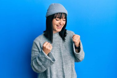 Yün kazak ve kış şapkası giyen genç İspanyol kadın kolları havada ve gözleri kapalı bir şekilde başarıyı kutluyor ve şaşırıyor. 