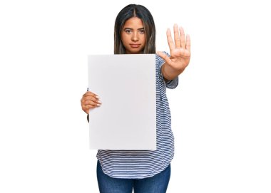 Elinde boş afiş tutan genç Latin kız elinde dur işareti yapıyor ciddi ve kendinden emin bir ifadeyle, savunma hareketi yapıyor. 
