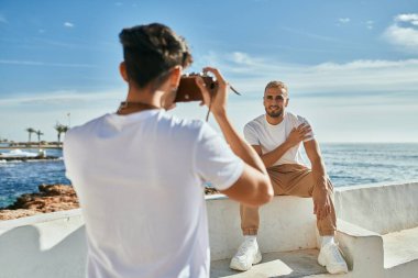 Denizin önünde erkek arkadaşının fotoğraflarını çeken bir adam..