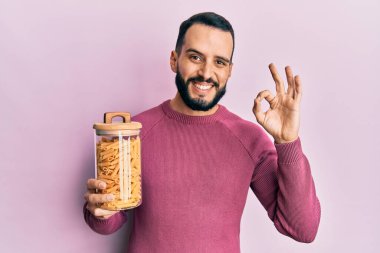 Sakallı genç adam elinde makarna kavanozuyla tamam işareti yapıyor, gülümsüyor ve mükemmel bir sembol. 