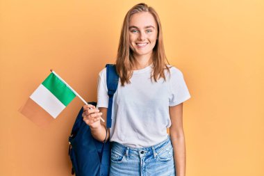 Güzel sarışın değişim öğrencisi. Elinde İrlanda bayrağı var. Olumlu ve mutlu görünüyor. 