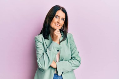 Orta yaşlı esmer kadın gündelik kıyafetler giyiyor kameraya kendinden emin bakıyor kollarını kavuşturmuş ve çenesini kaldırmış gülümsüyor. Olumlu düşünmek. 