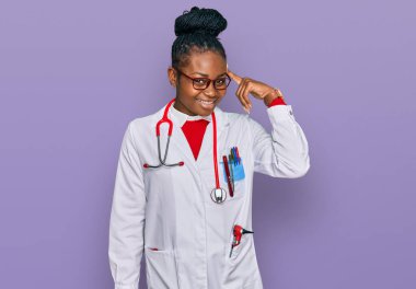 Genç Afro-Amerikan kadın doktor üniforması ve steteskop ile gülümseyerek tek parmağıyla, harika bir fikir ya da düşünceyle, iyi bir hafızaya sahip. 