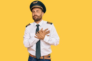 Sakallı, uçak pilotu üniforması giyen, elleri göğsünde, gözleri kapalı ve yüzünde minnet ifadesi olan yakışıklı bir adam. sağlık kavramı. 