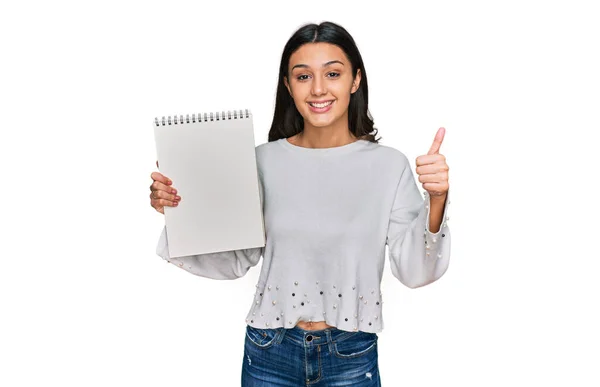 Joven Chica Hispana Sosteniendo Cuaderno Sonriendo Feliz Positivo Pulgar Hacia —  Fotos de Stock