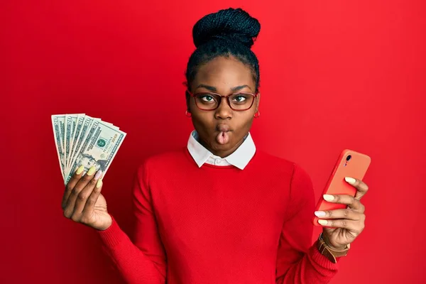 Joven Mujer Afroamericana Usando Smartphone Sosteniendo Dólares Haciendo Cara Pez —  Fotos de Stock