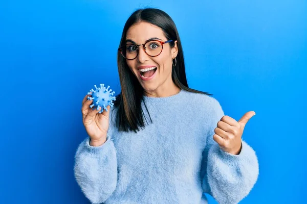 Young Brunette Woman Holding Virus Toy Pointing Thumb Side Smiling — Stockfoto