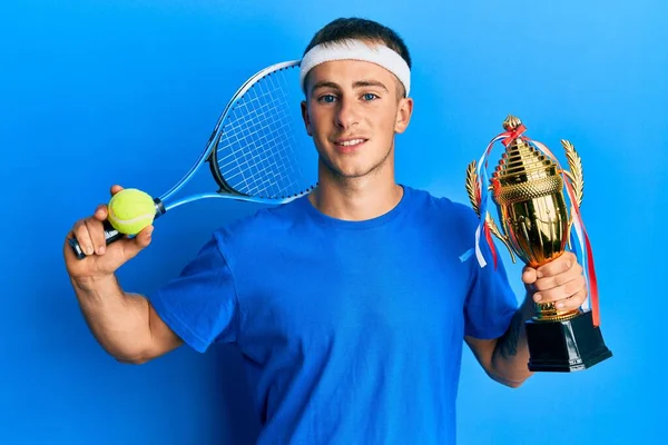 若い白人男性が笑顔で笑顔でトロフィーを掲げてテニスをしています 歯を見せて — ストック写真