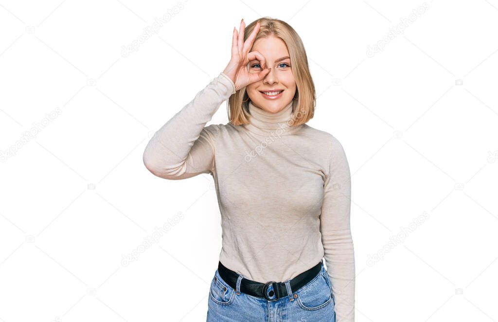 Young blonde woman wearing casual clothes doing ok gesture with hand smiling, eye looking through fingers with happy face. 
