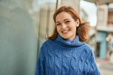 Genç beyaz kız gülümseyerek şehirde mutlu mesut duruyor..