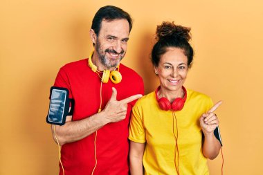 Orta yaşlı bir çift İspanyol kadın ve erkek spor giysisi ve kolluk takıyor. Yüzünde mutlu ve doğal bir ifadeyle gülümseyen bir yüz ifadesi var. 