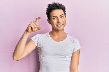 Genç, yakışıklı, günlük beyaz tişört giyen, gülümseyen, kendine güvenen, el hareketi yapan, parmaklarıyla işaret eden ve kameraya bakan bir adam. ölçüm kavramı. 