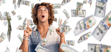 Yaz stili giyinmiş genç İspanyol adam şaşırmış ve şaşırmış bir şekilde yukarı bakıyor ve parmaklarıyla işaret ediyor ve kollarını kaldırıyor..