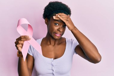 Elinde pembe kanser kurdelesi olan Afro-Amerikalı genç bir kız. Elleri havada, şaşırmış ve sinirli bir halde. 