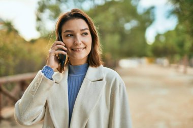 Genç İspanyol kadın gülümsüyor. Parktaki akıllı telefondan konuşarak mutlu oluyor..
